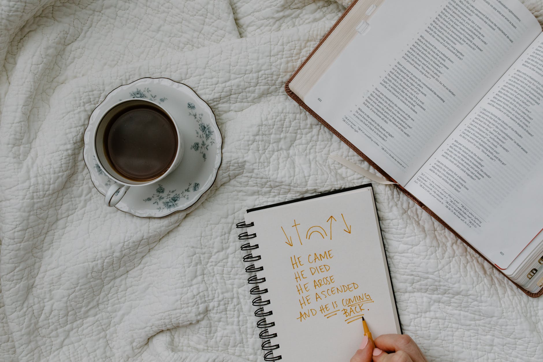 a person writing on the notebook beside a book and coffee